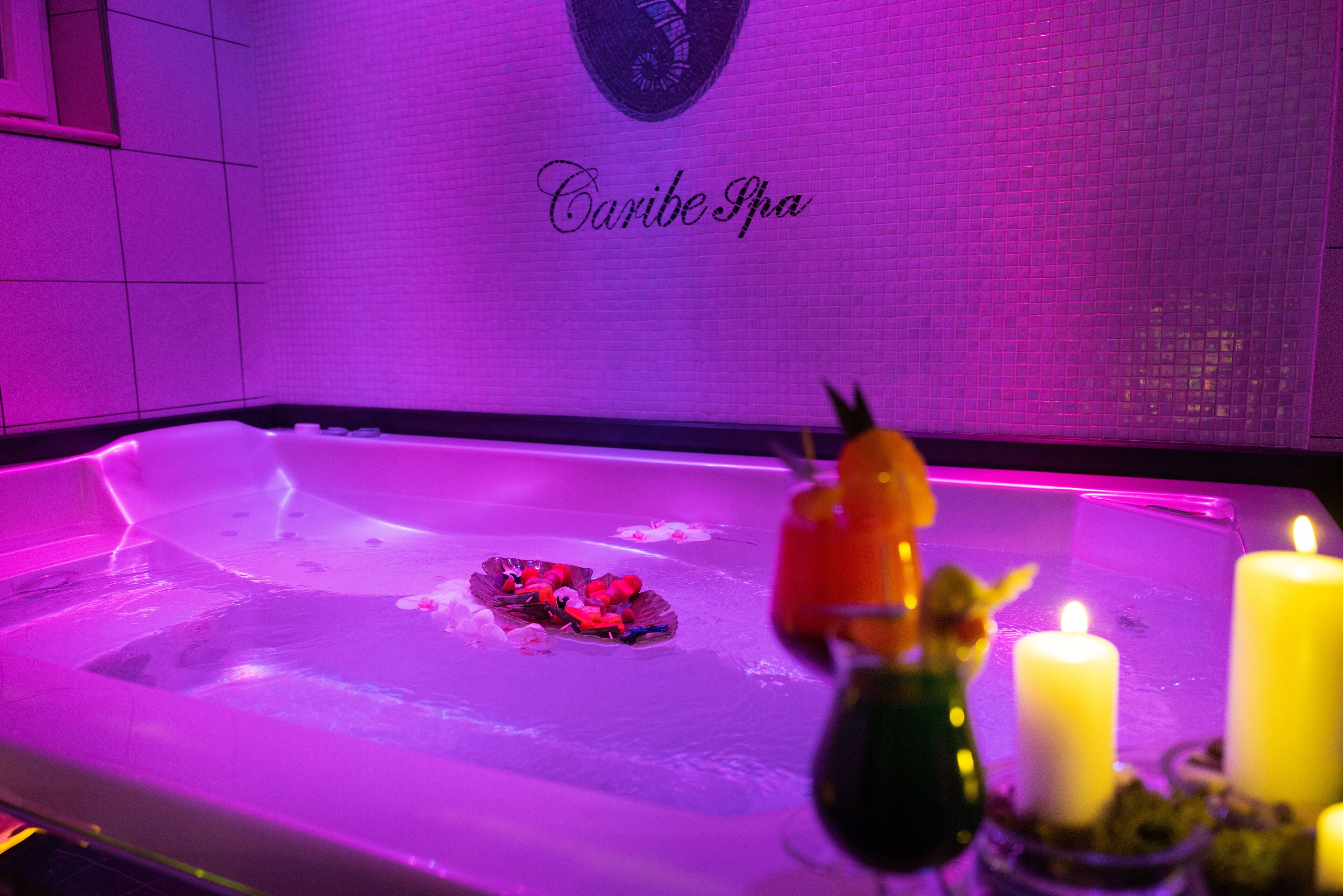 A spa area with a tub, candles, and decorative flowers.