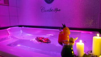 A spa area with a tub, candles, and decorative flowers.