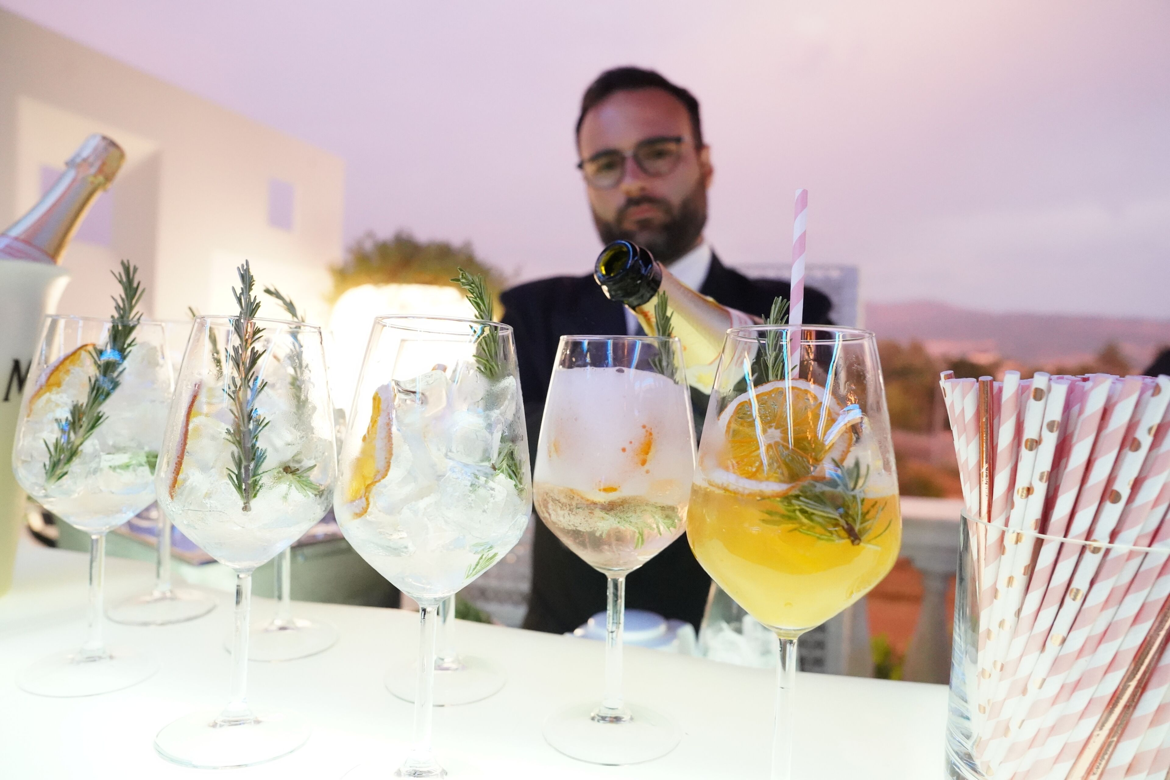 A bar setting with multiple glasses of cocktails, some with ice and garnishes, and a bottle being poured.