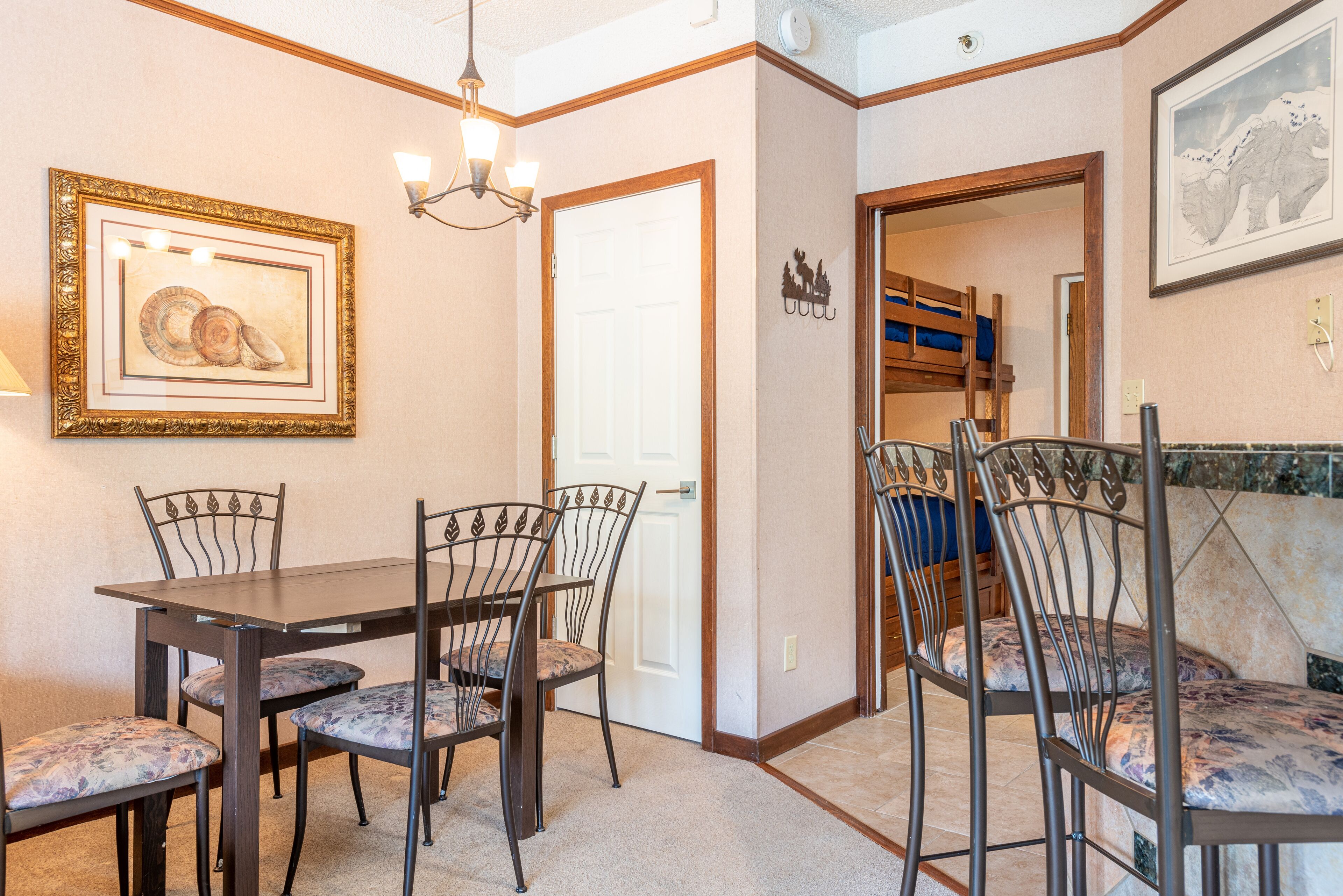A dining area with a table and chairs, a chandelier, and a door leading to a bunk bed room.