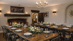Une salle à manger élégante, avec une longue table en bois dressée pour un repas, entourée de chaises, et une cheminée en arrière-plan.