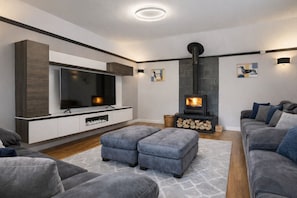 Een moderne woonkamer met een flatscreen televisie, een open haard, grijze banken en een groot tapijt.