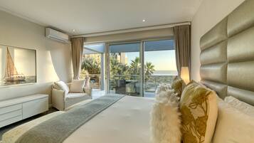 Una habitación de hotel moderna con una cama grande, un sofá y un balcón con vistas a palmeras y edificios.