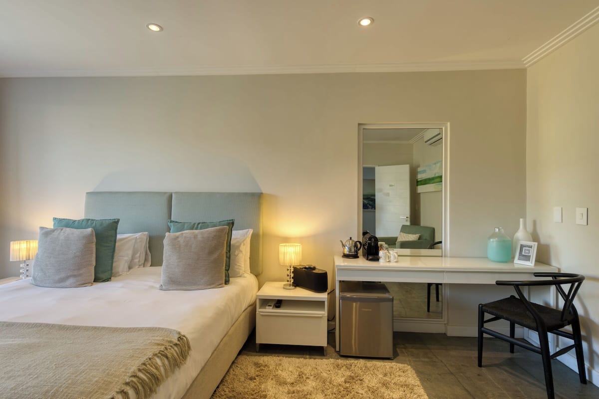 A hotel room with a bed, nightstands, a desk, a chair, a mirror, and a trash bin.