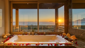 A large bathtub with rose petals and candles, a view of the ocean, and a balcony with a railing. - Atlantic Palms (Cape Town)