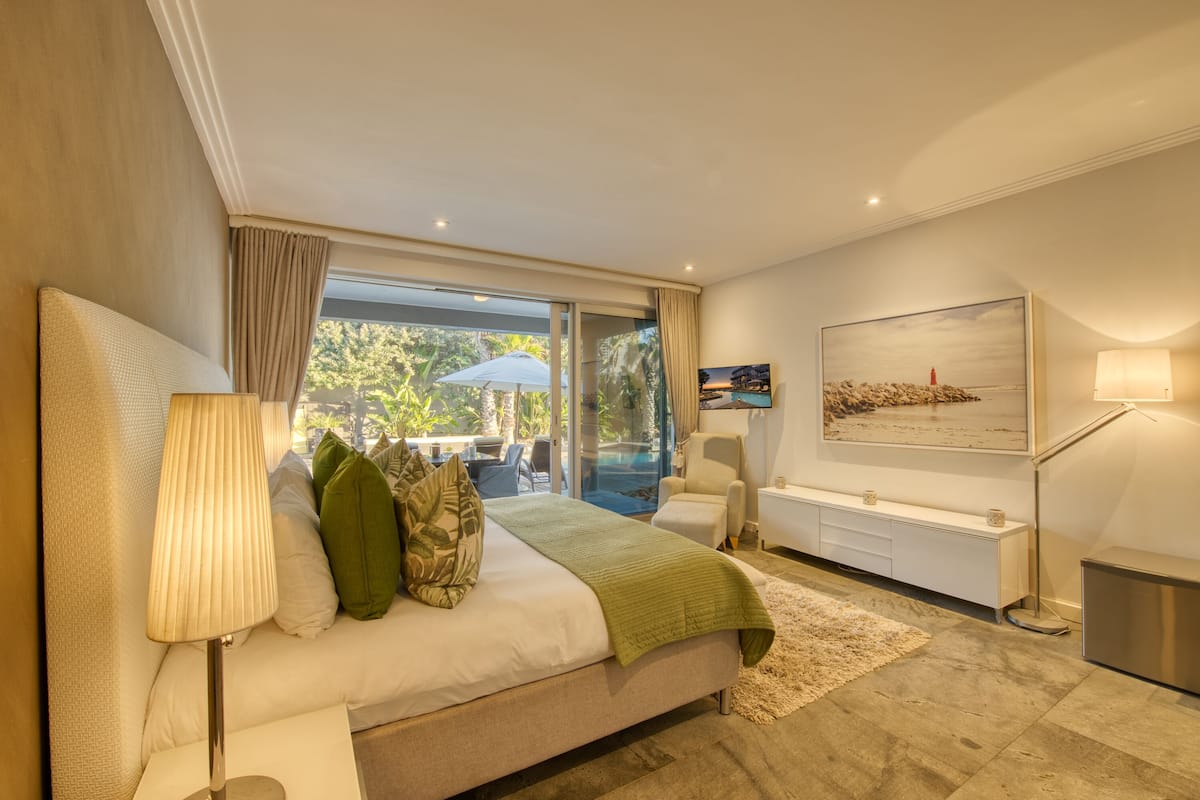 A modern bedroom with a large bed, a TV, a desk, and a view of the outdoors.