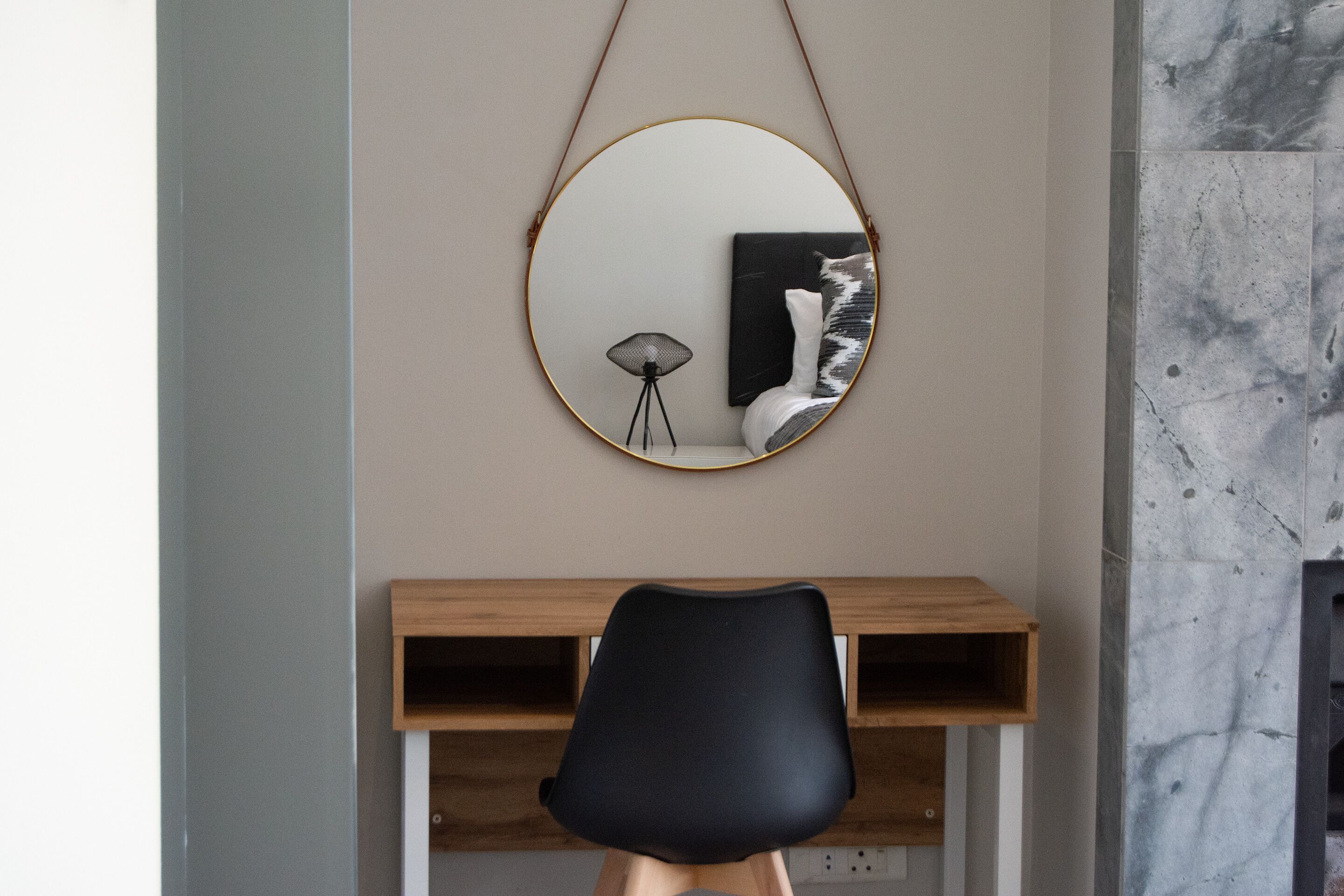 Una habitación moderna con un espejo redondo, un escritorio de madera y una silla negra.