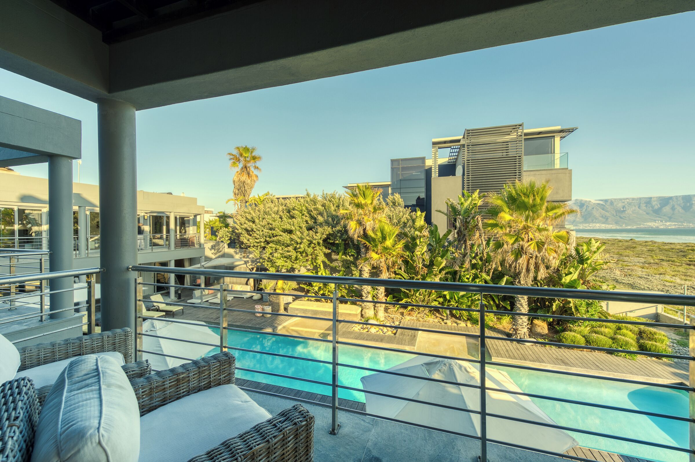 A rooftop pool area with lounge chairs, a swimming pool, and a view of a modern building and mountains.