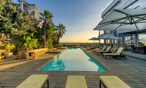 A pool area with lounge chairs and umbrellas, surrounded by greenery and overlooking a distant landscape. - Atlantic Palms (Cape Town)