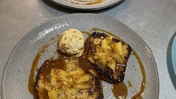 Dos tostadas con cobertura de caramelo y manzana, y una bola de helado sobre una mesa.