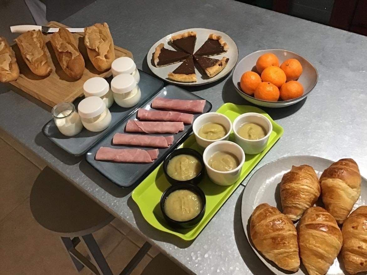 A breakfast spread with croissants, ham, chocolate tart, oranges, and various dips on a table.
