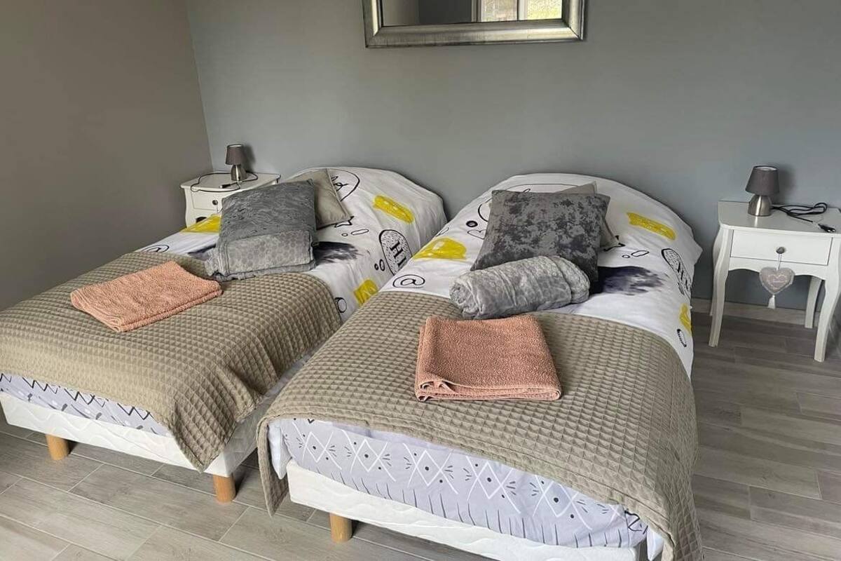 A room with two beds, each with a patterned bedspread and pillows, a bedside table with a lamp, and a mirror on the wall.