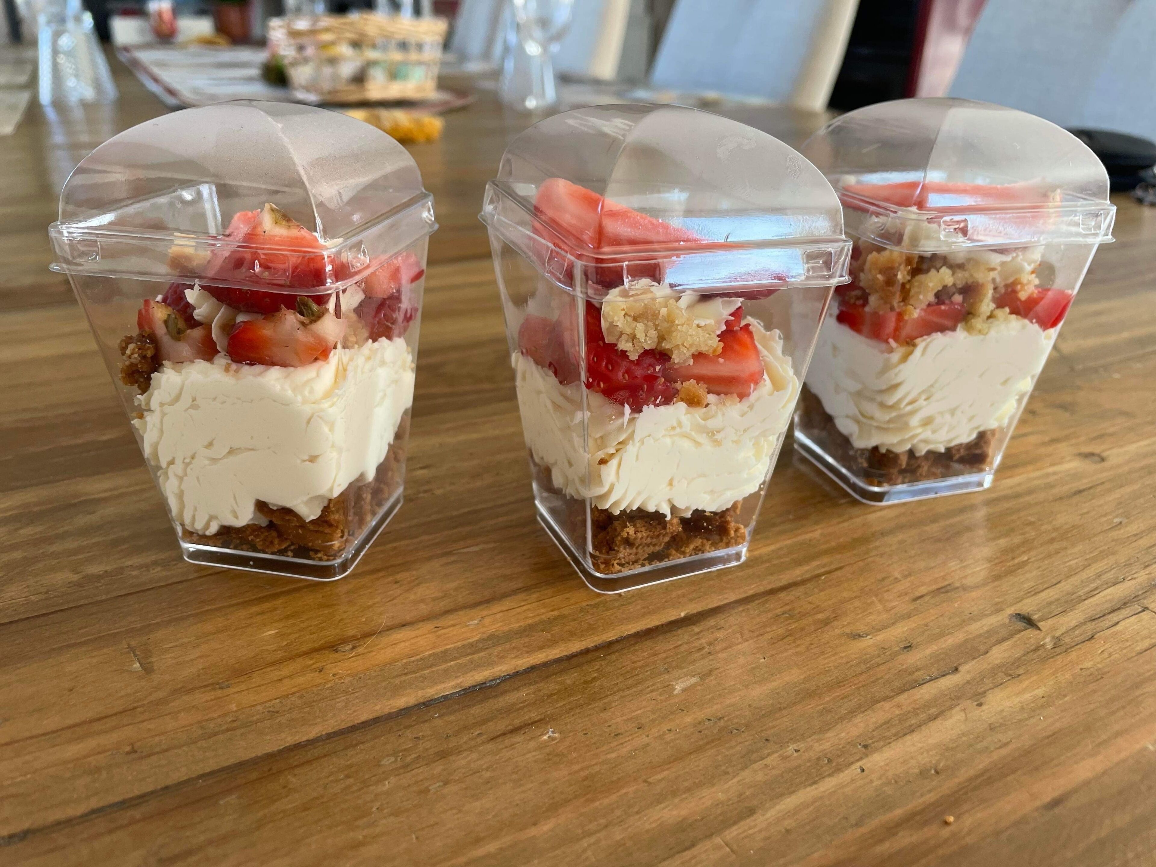 Three dessert cups with a clear plastic dome on top, placed on a wooden table.