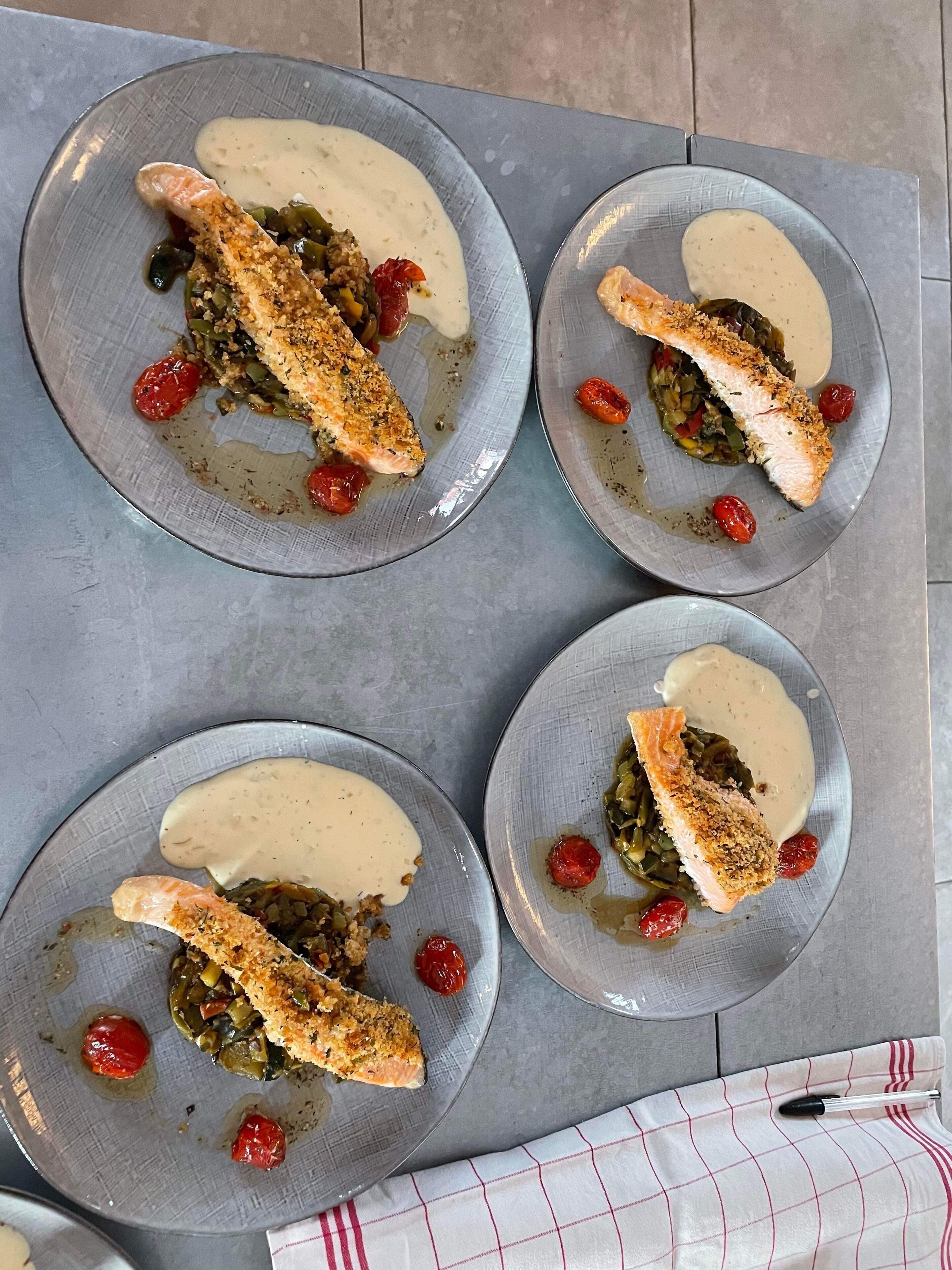 Four plates of food with salmon, vegetables, and a creamy sauce.
