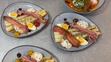 Cuatro platos de comida con tocino, huevos y aceitunas sobre una mesa de metal.