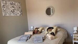 A neatly made bed with a beige blanket, pillows, and a decorative mirror above it. - La Petite Salamandre (Chitenay)
