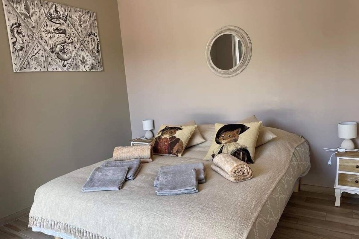 A neatly made bed with a beige blanket, pillows, and a decorative mirror above it.