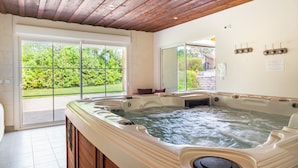 A spa room with a hot tub, wooden ceiling, sliding glass doors to a garden, and a view of greenery.
