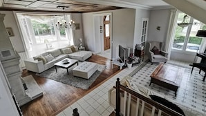 A spacious living room with a sectional sofa, a coffee table, and a TV stand. There is a staircase leading to an upper level.