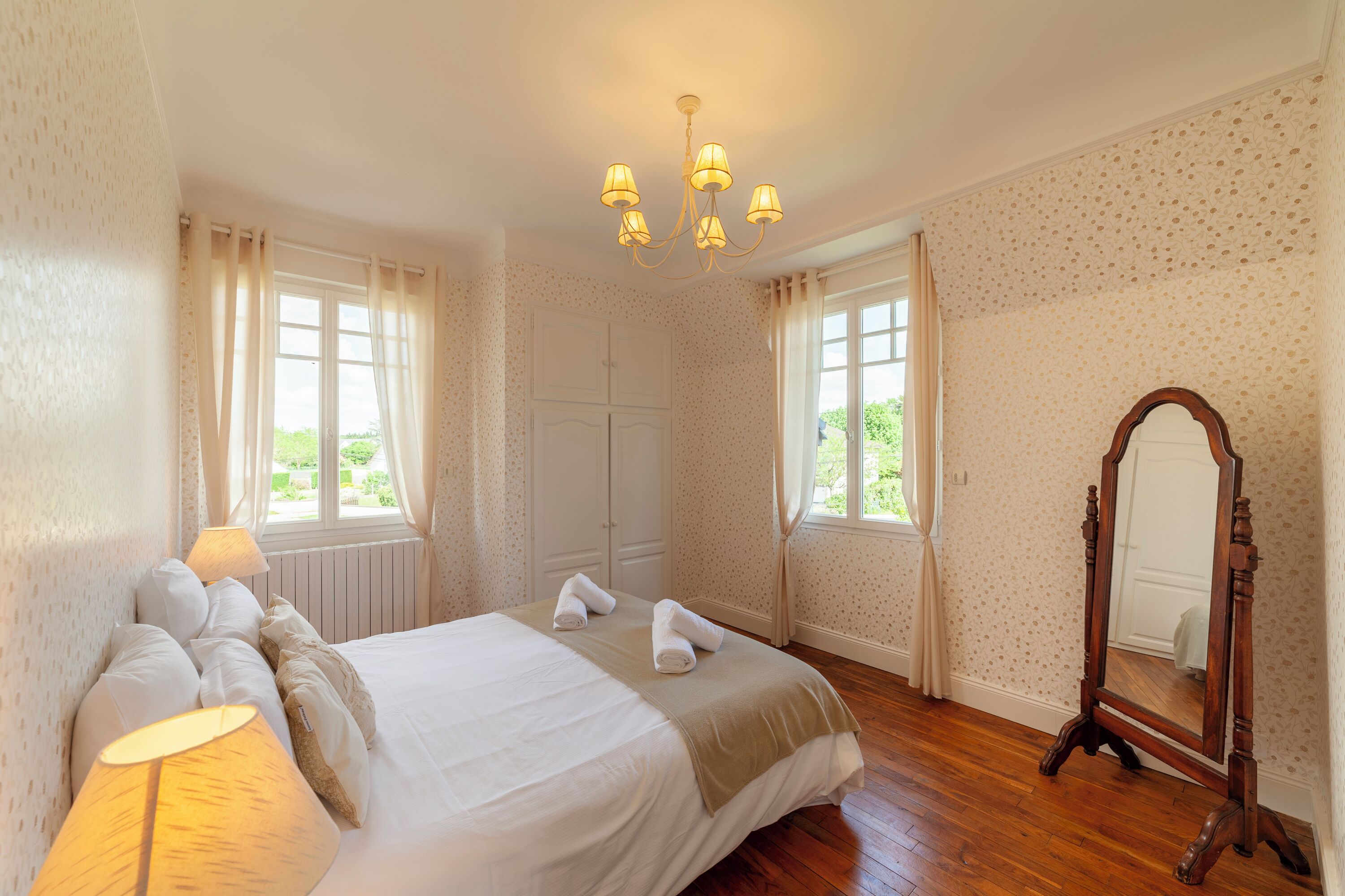 A bedroom with a large bed, two bedside lamps, a wooden dresser, and a mirror.