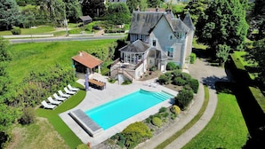 A large house with a swimming pool, a covered patio, and a well-maintained lawn.