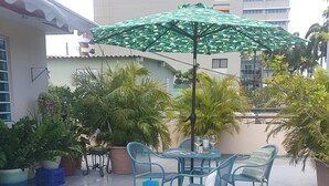An outdoor patio with a table and chairs, surrounded by potted plants and a green umbrella.