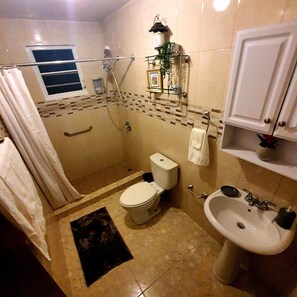 A bathroom with a shower, toilet, sink, and a small window.