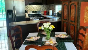 A modern kitchen with a refrigerator, stove, and sink, a dining table with chairs, and a decorative cabinet.