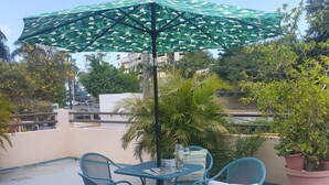 A patio with a table and chairs, a green umbrella, and potted plants.