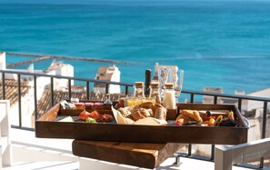 Un plateau de petit-déjeuner avec des viennoiseries, des fruits et des boissons, posé sur un balcon donnant sur la mer.