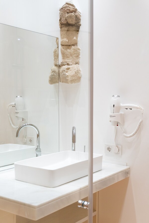 Une salle de bain avec un lavabo blanc, un miroir, un sèche-cheveux et un élément décoratif en pierre sur le mur.
