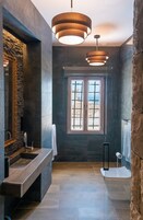 Un baño moderno con pared de piedra, un espejo grande, tocador de madera y ventana con vistas.