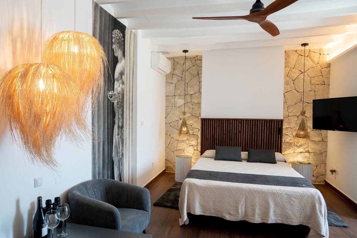 A modern bedroom with a bed, a chair, a TV, and a ceiling fan.