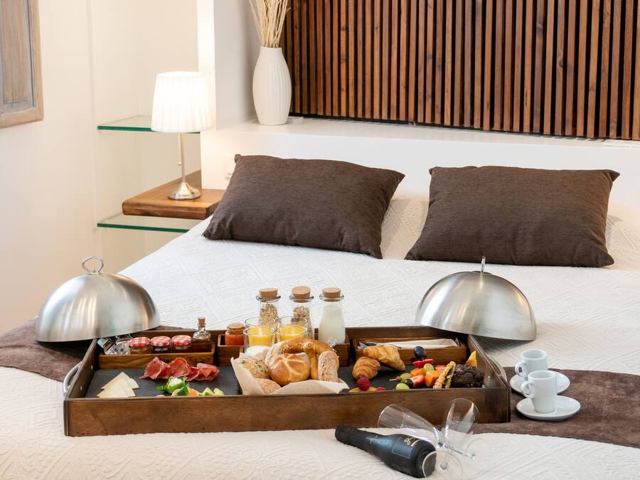 Una cama bien hecha con una bandeja de desayuno, almohadas y una lámpara de noche.