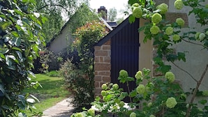 Een gebouw van steen met een donker dak, omgeven door weelderige begroeiing en een stenen pad.