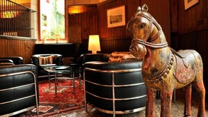 Een hal met lederen banken, een zwart, rond poef, een paardenbeeld, een lamp en een trap.