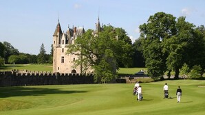 Een kasteel met een gracht en een golfbaan op de voorgrond.