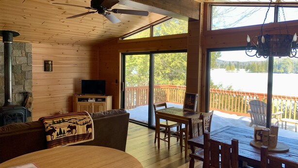 Ein gemütliches Blockhaus-Interieur mit Kamin, Deckenventilator, Fernseher und Essbereich mit Tisch und Stühlen.