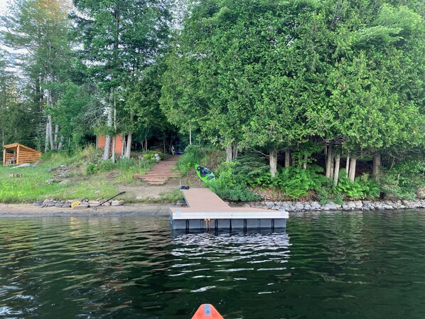Ein Steg, der sich in einen ruhigen Fluss erstreckt, umgeben von dichtem Grün und einer hölzernen Struktur im Hintergrund.