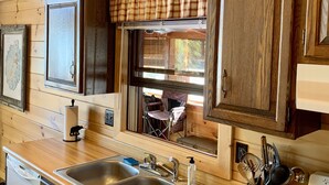 Eine Küche mit Holzausstattung, einem Spülbecken mit zwei Mulden und einem Fenster mit Blick auf einen Außenbereich mit Sitzgelegenheiten.