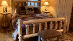 Ein gemütliches Schlafzimmer in einer Blockhütte mit einem hölzernen Bett, zwei Nachttischlampen, einer karierten Bettdecke und einer Bank.