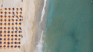 Vue aérienne d’une plage avec des rangées de parasols et des personnes se prélassant au soleil.
