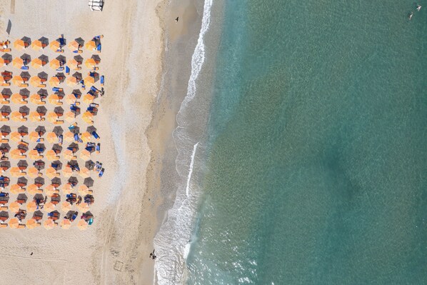 An aerial view of a beach with rows of umbrellas and beachgoers.