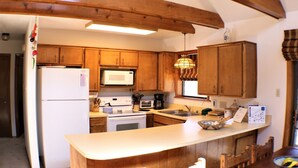 Une cuisine avec des meubles en bois, un réfrigérateur blanc, un four à micro-ondes, une cuisinière et une machine à café.
