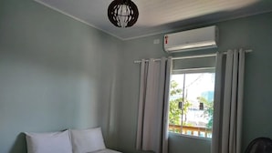 A bedroom with a bed, a window with curtains, an air conditioning unit, and a fan. - Naldo Ilha Bela (Ilhabela)