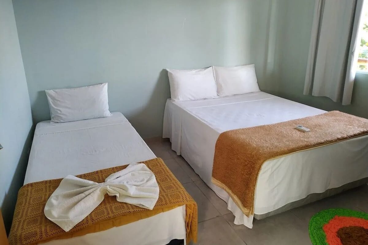 A hotel room with two single beds, a small table with a towel, and a green and red rug.