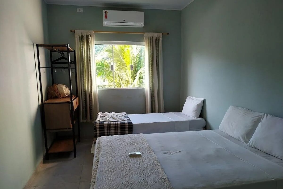 A compact hotel room with two beds, a small seating area, and a window with curtains.
