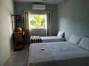 Une chambre d’hôtel de taille réduite, comprenant deux lits, un petit coin salon et une fenêtre avec des rideaux.