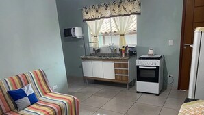 A compact living space with a striped sofa, a kitchenette with a stove, and a small table. - Naldo Ilha Bela (Ilhabela)