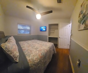 Une chambre à coucher comprenant un lit, un ventilateur de plafond, un téléviseur et une porte donnant sur une autre pièce.